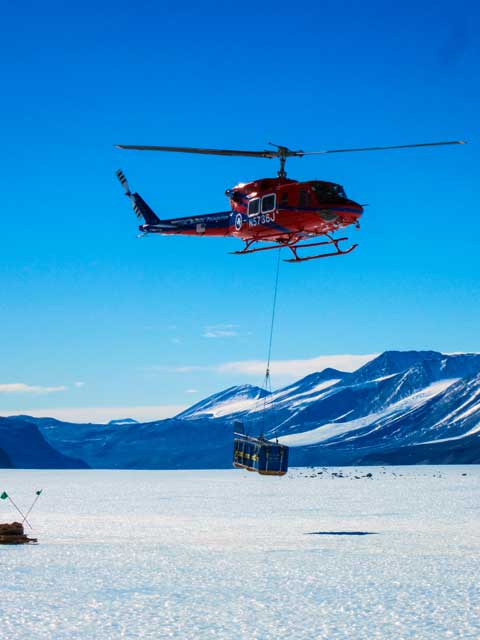 A helicopter carries away a load of ice cores from the field camp on Taylor Glacier to McMurdo Station
